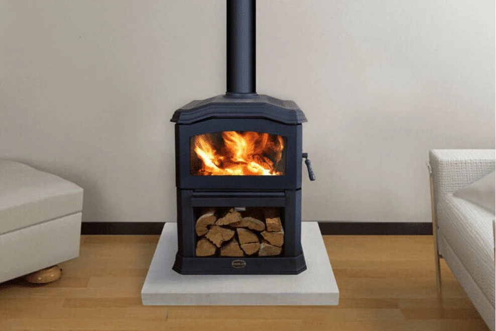 Wood-burning stove with flames and logs inside, placed on a white platform in a room with light-colored walls and furniture.
