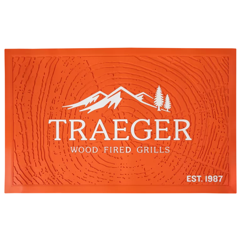 Traeger grill mat for BBQ accessories, showing a black, non-slip grill mat in front of a Traeger grill for protection and grilling convenience.